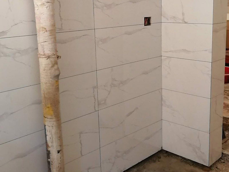 衛(wèi)生間瓷磚鋪貼：基層處理：首先應(yīng)除去基層表面的污垢，油漬，浮灰;除去基層上所有涂料層，膩?zhàn)訉?如果基層未能達(dá)到平整度要求，需對(duì)基層進(jìn)行預(yù)先的找平處理。  放樣：鋪貼瓷磚前需事先找好垂直線，以此為基準(zhǔn)鋪貼的瓷磚高低均勻、垂直美觀;此外，施工前在墻體四周需彈出標(biāo)高控制線，在地面彈出十字線，以控制地磚分隔尺寸。  預(yù)鋪：首先應(yīng)對(duì)瓷磚的色彩、紋理、表面平整等進(jìn)行嚴(yán)格的挑選，然后按照?qǐng)D紙要求預(yù)鋪。 調(diào)制粘結(jié)劑：加水后將粘結(jié)劑漿料攪拌至潤(rùn)滑均勻，無(wú)明顯塊狀或糊狀結(jié)塊，攪拌后的漿料靜置5-10分鐘后再稍加攪拌1-2分鐘即可使用。在開(kāi)始鋪貼施工前，需要先清理瓷磚表面的浮灰，污垢等。  抹漿料：將調(diào)制好的漿料均勻地抹在瓷磚背面，要求漿料飽滿。將瓷磚平整地鋪貼在基層上，使用橡膠錘將瓷磚拍實(shí)鋪平。施工過(guò)程中，可小幅度轉(zhuǎn)動(dòng)瓷磚，使?jié){料與瓷磚背面充分接觸。 瓷磚鋪貼結(jié)束后24小時(shí)，可進(jìn)行嵌縫施工。將調(diào)制好的嵌縫劑均勻地涂在磚與磚的縫隙內(nèi)。嵌縫后用浸濕的織物清理多余的嵌縫劑，保持瓷磚表面清潔。