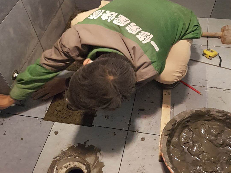 廁所貼地磚： 1、基層處理：把沾在基層上的浮漿、落地灰等用暫子或鋼絲刷清理掉，再用掃帚將浮土清掃干凈。 2、找標高：根據水平標準線和設計厚度，在四周墻、柱上彈出面層的上平標高控制線。 3、排磚：將房間依照磚的尺寸留縫大小，排出磚的放置位置，并在基層地面彈出十字控制線和分格線。 4、鋪設結合層砂漿：鋪設前應將基底濕潤，并在基底上刷一道素水泥漿或界面結合劑，隨刷隨鋪設攪拌均勻的干硬性水泥砂漿。 5、鋪磚：將磚放置在于拌料上，用橡皮錘找平，之后將磚拿起，在干拌料上澆適量素水泥漿，同時在磚背面涂厚度約lnm的素水泥膏，再將磚放置在找過平的干拌料上，用橡皮錘按標高控制線和方正控制線坐平坐正。 6、鋪磚時應先在房間中間按照十字線鋪設十字控制磚，之后按照十字控制磚向四周鋪設，并隨時用2m靠尺和水平尺檢查平整度。大面積鋪貼時應分段、分部位鋪貼。 7、養(yǎng)護：當磚面層鋪貼完24h內應開始澆水養(yǎng)護，養(yǎng)護時間不得小于7d。