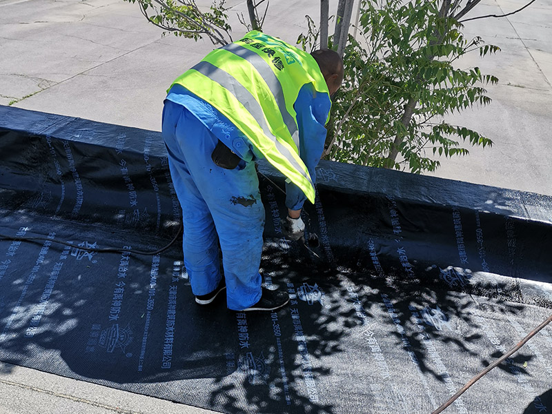 屋頂防水卷材鋪貼:清除基層表面雜物、油污、砂子，凸出表面的石子、砂漿疙瘩等應(yīng)清理干凈，清掃工作必須在施工中隨時進行，并修補平整表面。尤其鏟除排水口、煙囪、管壁上的水泥砂漿等附著物；根據(jù)施工現(xiàn)場狀況，進行合理定位，確定卷材鋪貼方向，在基層上彈好卷材控制線，依循流水方向從低往高進行卷材試鋪。卷材試鋪后，先將要鋪貼的卷材剪好，反鋪于基面上(即是底部隔離紙朝上)，撕剝?nèi)ゾ聿母綦x紙。撕剝時，已剝開的隔離紙宜與粘結(jié)面保持45～60度的銳角，防止拉斷隔離紙，盡量保持在自然松弛狀態(tài)，但不要有皺折。