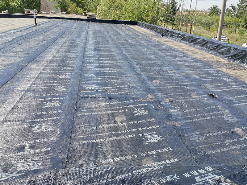 屋頂防水卷材鋪貼:清除基層表面雜物、油污、砂子，凸出表面的石子、砂漿疙瘩等應(yīng)清理干凈，清掃工作必須在施工中隨時進行，并修補平整表面。尤其鏟除排水口、煙囪、管壁上的水泥砂漿等附著物；根據(jù)施工現(xiàn)場狀況，進行合理定位，確定卷材鋪貼方向，在基層上彈好卷材控制線，依循流水方向從低往高進行卷材試鋪。卷材試鋪后，先將要鋪貼的卷材剪好，反鋪于基面上(即是底部隔離紙朝上)，撕剝?nèi)ゾ聿母綦x紙。撕剝時，已剝開的隔離紙宜與粘結(jié)面保持45～60度的銳角，防止拉斷隔離紙，盡量保持在自然松弛狀態(tài)，但不要有皺折。