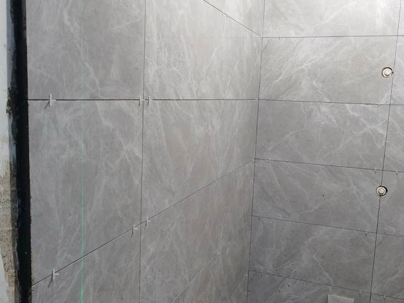 衛(wèi)生間貼磚施工：應(yīng)全部清理墻面上的各類污物，打掃干凈現(xiàn)場，特別是腳落里。用泥刀先批墻，后用水泥漿找平。這個工序很重要，確保底子平，防止貼后空鼓。墻面要刷防水涂料，防止貼后浸水，一般高度不低于1.8米，刷的時候會稍高一些。根據(jù)設(shè)計鋪貼圖樣的要求，確定排磚方案，用墨斗彈線，以減少施工損耗。把剛剛攪拌好的粘結(jié)劑漿料均勻的刮到墻上。瓷磚上墻將經(jīng)過預(yù)先清潔的瓷磚平整地鋪貼在粘結(jié)劑漿料基層上，使用橡膠錘將瓷磚拍實鋪平。施工過程中，可小幅度轉(zhuǎn)動瓷磚，使?jié){料與瓷磚背面充分接觸。專家建議在鋪貼時，隨機(jī)取下已鋪貼于基層上的瓷磚作檢查。確保漿料與瓷磚背面的充分接觸。 留縫大小調(diào)整根據(jù)瓷磚的尺寸，在磚與磚之間預(yù)留相應(yīng)尺寸的縫隙留待嵌縫?？捎醚篮灥认裙潭?，粘結(jié)劑具有一定的可調(diào)整性，可對留縫的大小進(jìn)行調(diào)整。