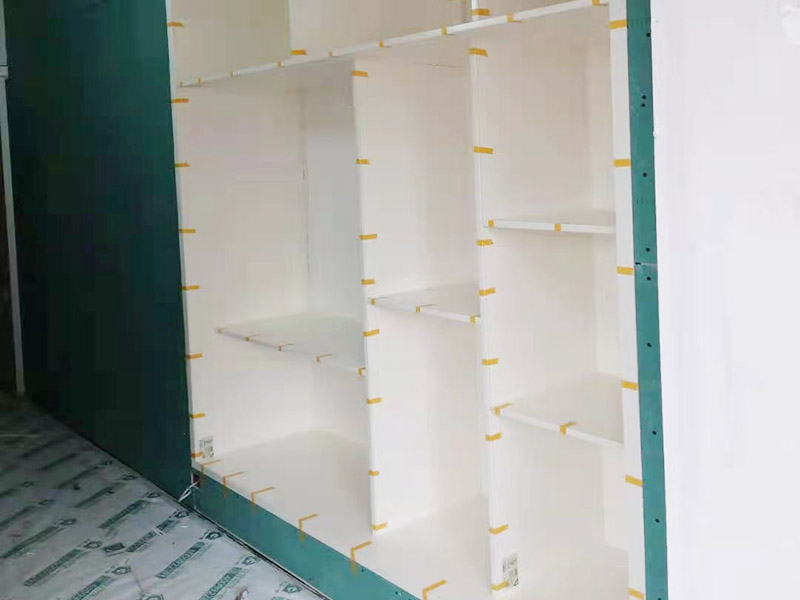 客廳定制柜體安裝：用墊布點(diǎn)好地板，先從靠墻的一端寬側(cè)板開始組裝，將寬側(cè)板平放于地面上（離后墻面保持700mm間隔）。首先將填好的三合一膠塞的板件，平放在墊布上，檢查孔距與圖紙相符，并裝上三合一單連桿。然后將固層釘上木塞，固定于寬側(cè)板上面，頂板大柄孔朝上，其余固層都朝下，腳線大柄孔朝內(nèi)（中間固層與L架高度一致，即底板到固層內(nèi)空為960mm，現(xiàn)場打?qū)影蹇祝?。放上?cè)板，釘上木塞，木塞要求連通兩邊的固層。在第二個柜固層上面裝好雙連桿，留意雙連桿上面大柄只能鎖住一半，即90&deg;。當(dāng)兩件固層與側(cè)板固定后再同時擰緊大柄。裝第三個柜時重復(fù)第二個柜的安裝步驟。