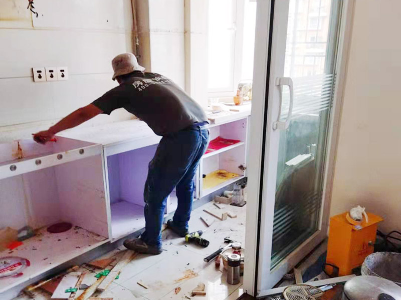 廚房櫥柜安裝：清理：對(duì)廚房作防護(hù)措施，掛擋布、廚房墻面等做簡(jiǎn)單清理，以便準(zhǔn)確測(cè)量地面水平。櫥柜安裝一般先從地柜開始。把櫥柜外包裝拆開后。在櫥柜的邊緣貼上防火膜封邊。在下柜底部安裝上支腳，根據(jù)地面水平高度調(diào)整櫥柜。 櫥柜安裝需要找出基準(zhǔn)點(diǎn)，L型廚房從直角處向兩邊延伸，U型廚房則先將中間的一字型柜體放整齊后，再?gòu)膬蓚€(gè)直角處向兩邊站看，這樣可以避免出現(xiàn)縫隙。櫥柜框架安裝牢固定位后，需要在櫥柜背面安裝背板。一般安裝下水都會(huì)現(xiàn)場(chǎng)開孔，工人會(huì)用專業(yè)的打孔器按照管道大小進(jìn)行打孔，打孔的直徑應(yīng)比管道大3-4毫米，并且打孔后要將開孔部分用密封條封邊，防止邊緣滲水木材變形。